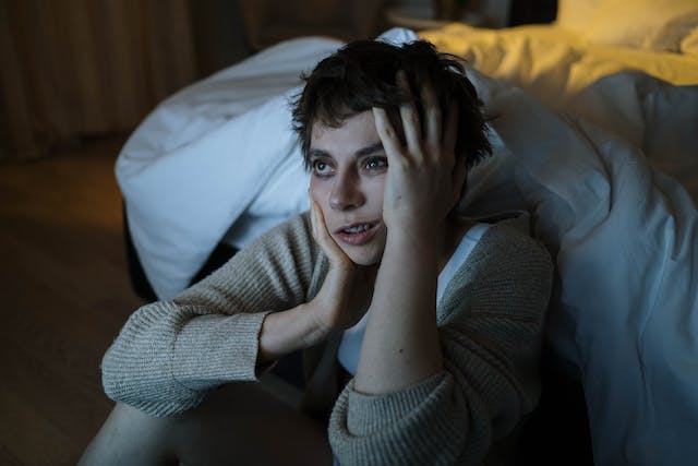 Tired woman sitting on the floor next to her bed.