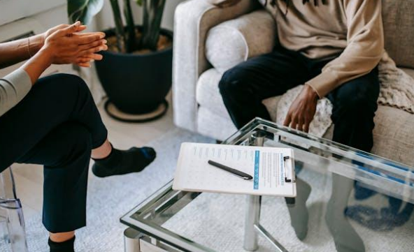 Two people sitting near a pen and a checklist, placed on a glass coffee table.