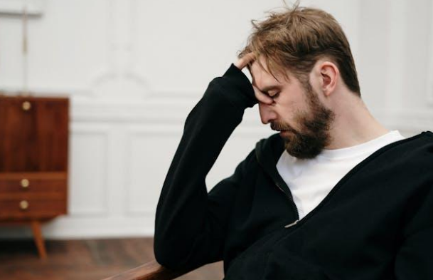 A man in a black sweater holding his head in silence.