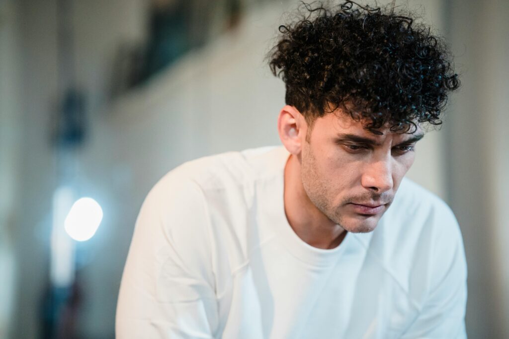 A stressed man in a white t-shirt, looking down.